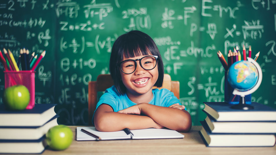 Ein lächelndes Schulmädchen sitzt am Tisch mit Büchern, Stiften und einer Weltkugel